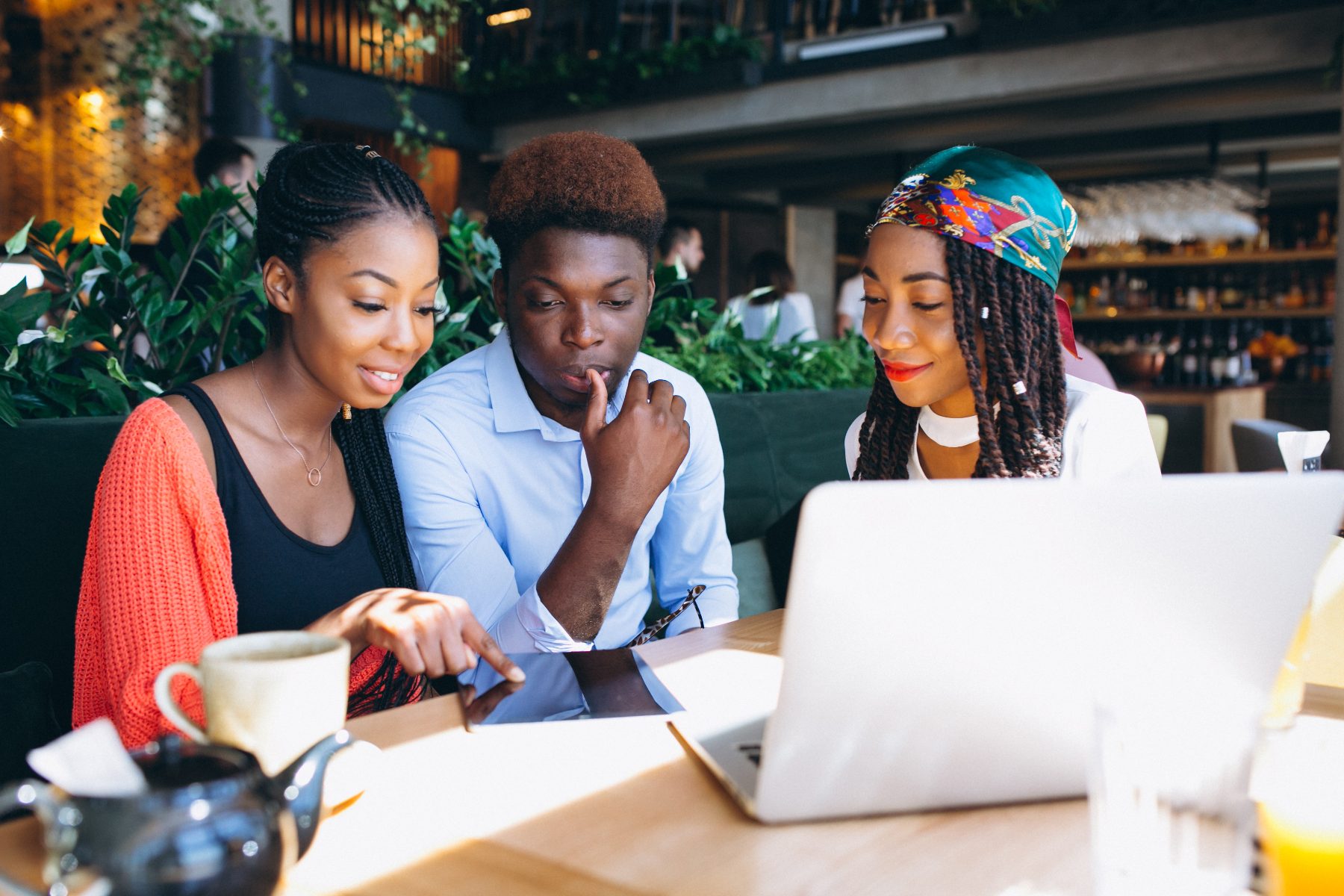 Three Black professionals reviewing work together on a laptop at a café table